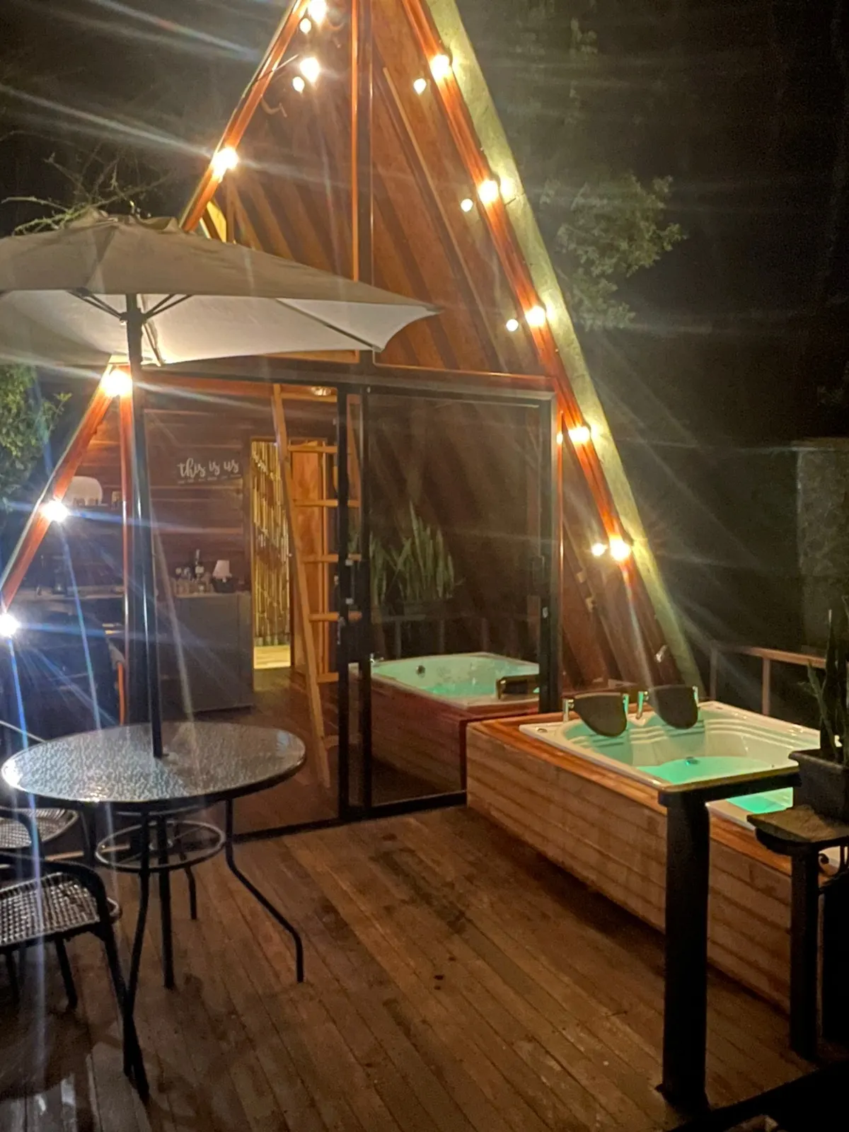 Cabaña Eucalipto en forma de A iluminada en la noche, con terraza, mesa y jacuzzi